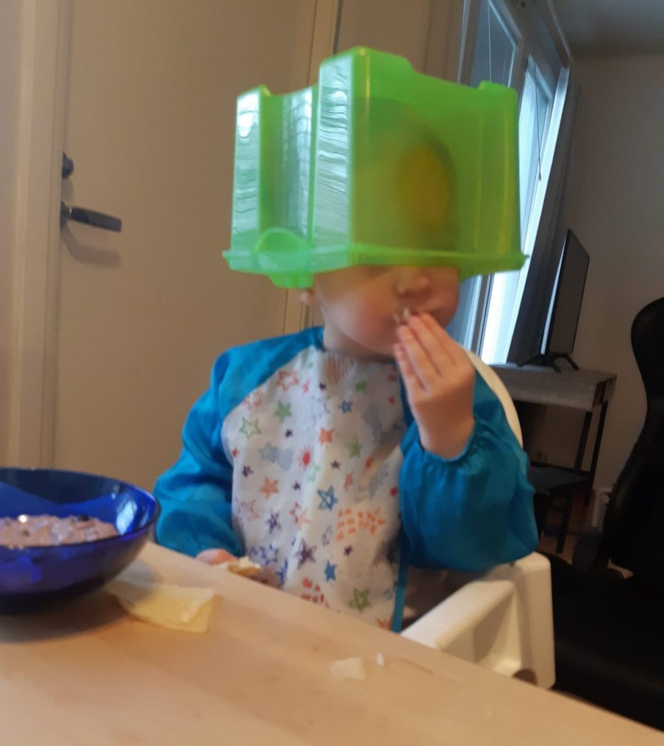 Lapsi dublolaatikko päässään ruokapöydässä.