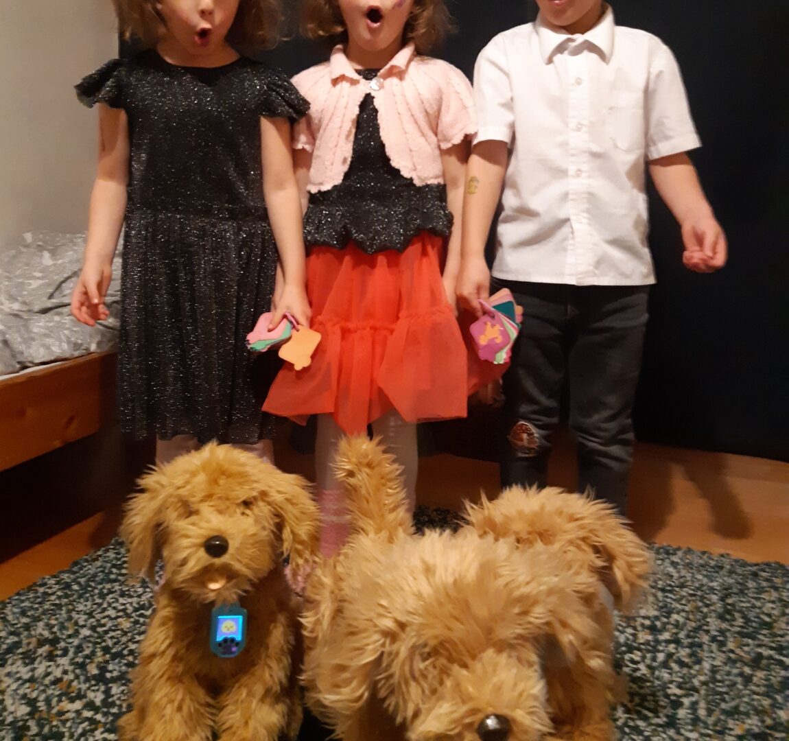 Kolme lasta juhlavaatteissa pehmolelukoirien kanssa.