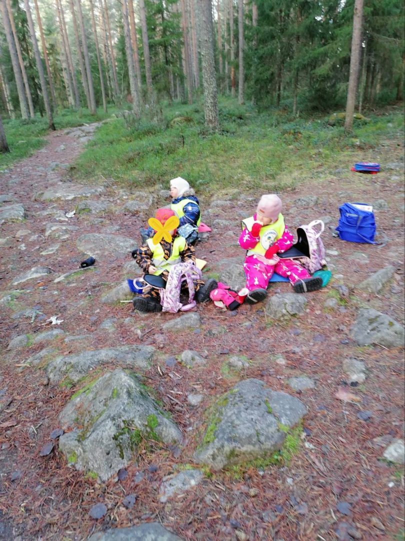 Kolme lasta istuu metsässä syömässä eväitä.