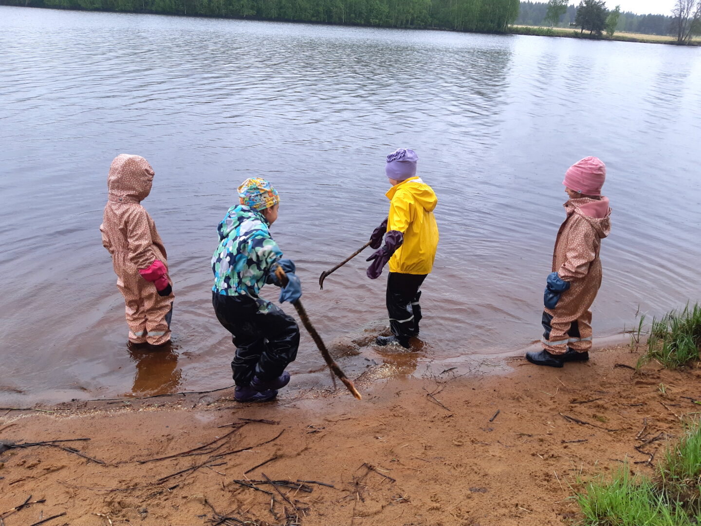 Neljä lasta joen rannassa sadeasuissa leikkimässä.