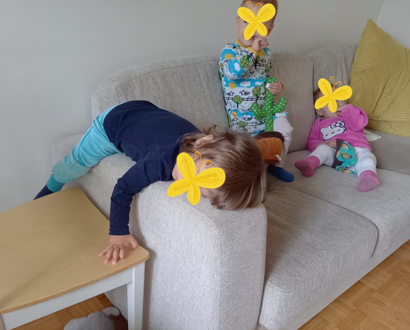Kolme taaperoa sohvalla loikoilemassa. Kasvot peitetty emojeilla.