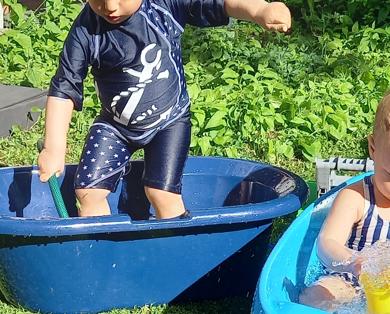Kaksi lasta ammeissa pihalla, rajattu niin etteivät kasvot näy.