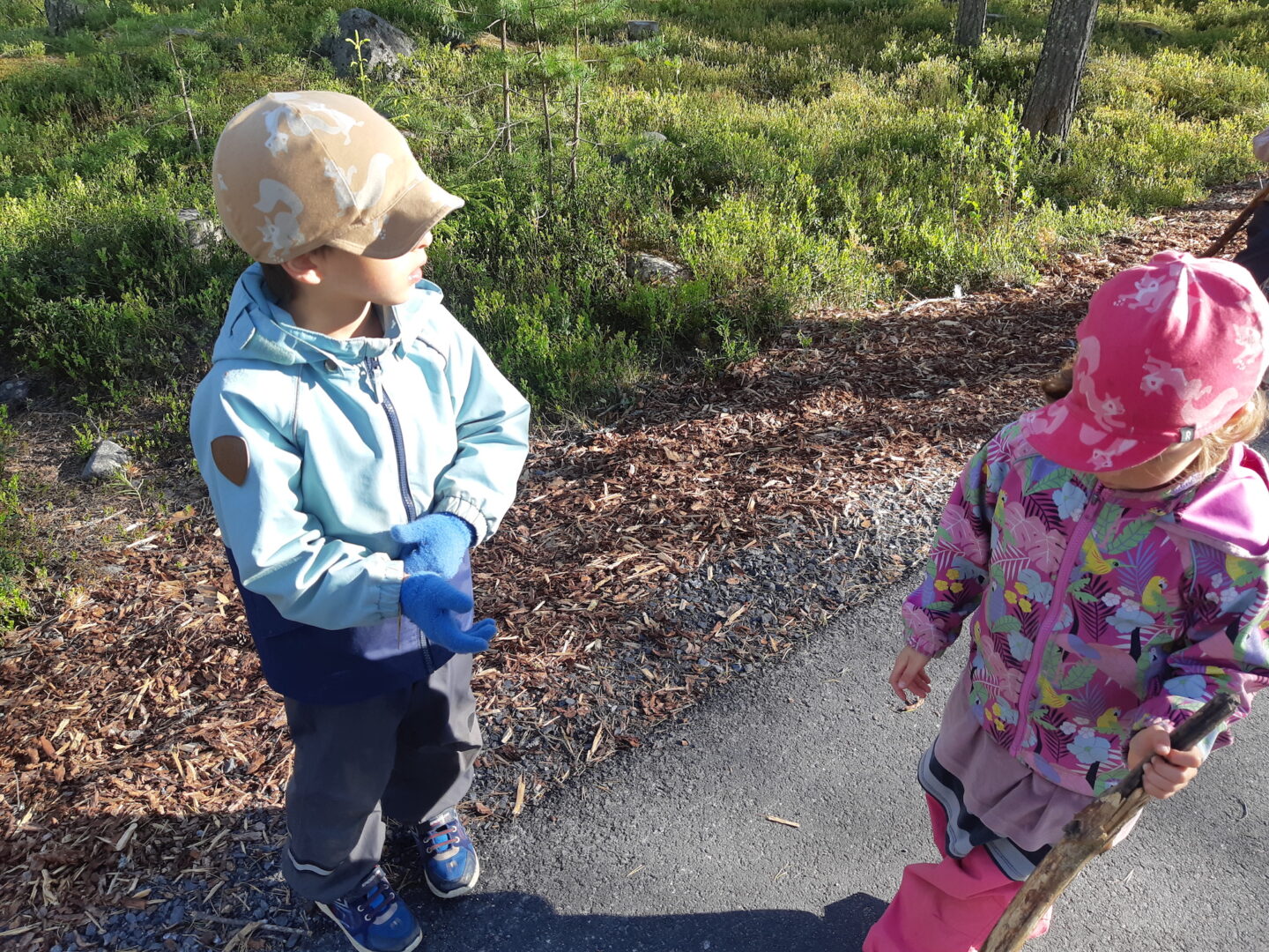 Kaksi lasta ulkona kävelyllä, toisella keppi kädessään.