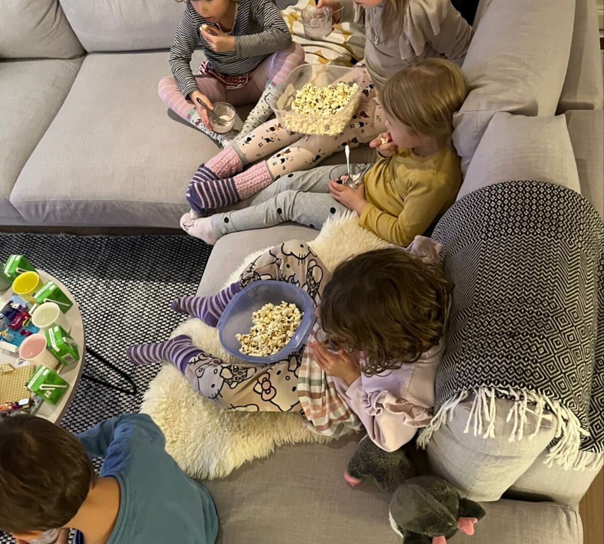 Viisi lasta sohvalla syömässä popcornia.