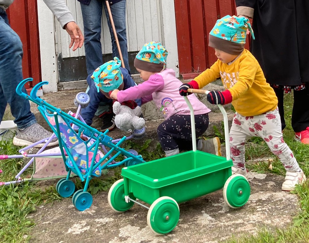 Kolme lasta mökin portaiden edustalla. Yksi työntää kärryä.