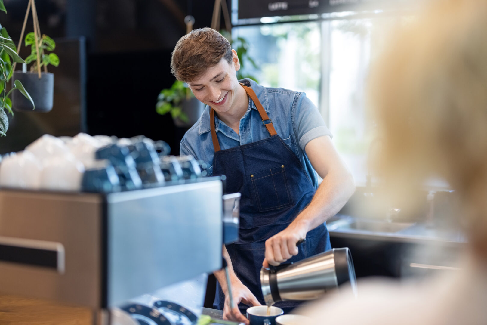Nuori barista kaataa kahvia kuppiin asiakkaalle.