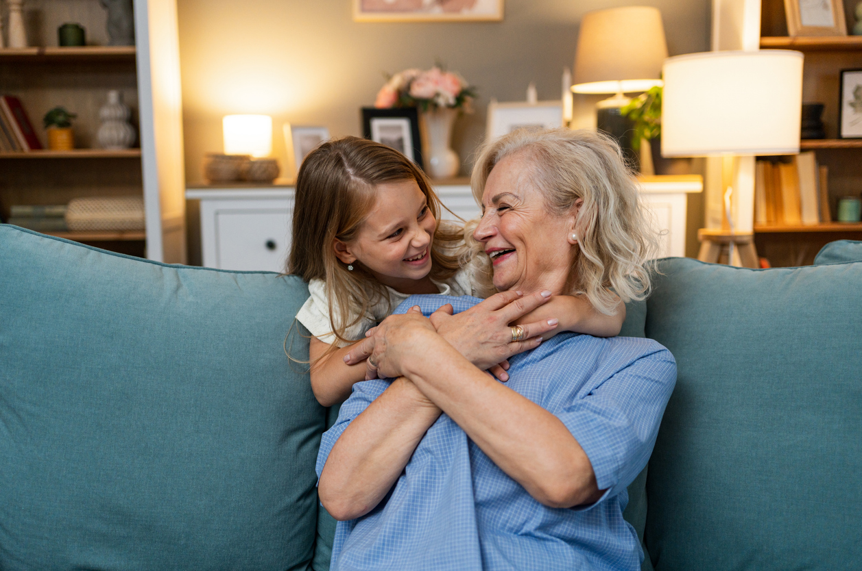 Tyttö halaa sohvalla istuvaa isoäitiään. Molemmat hymyilevät iloisesti.
