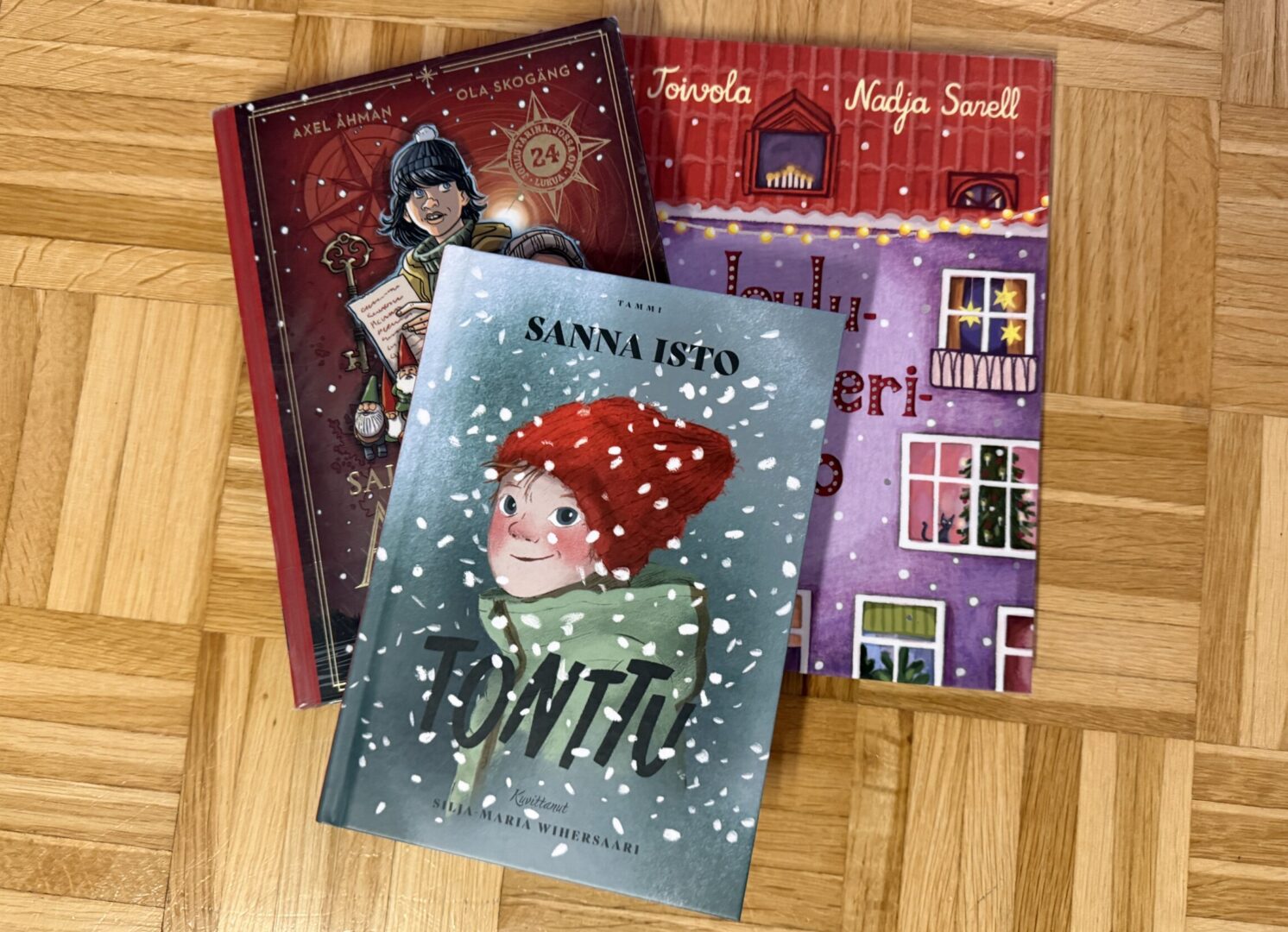 Kolme jouluista kirjaa limittäin lattialla.