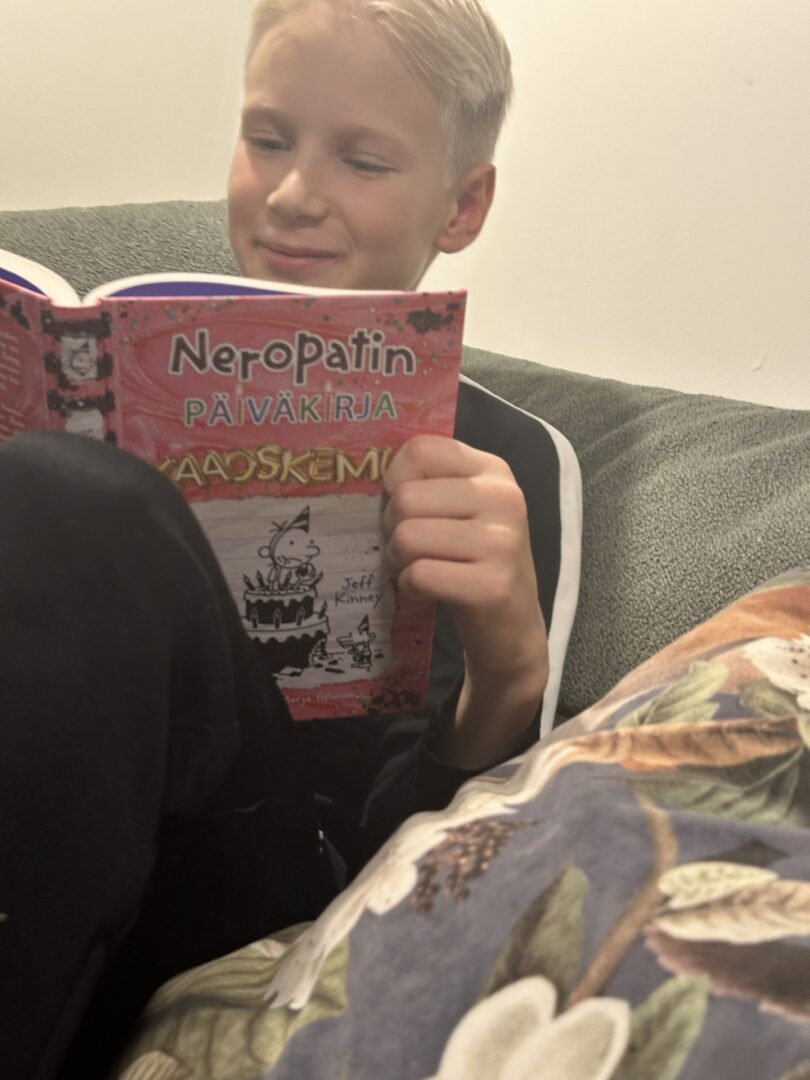 Poika lukee sohvalla Neropatin päiväkirjaa ja hymyilee.