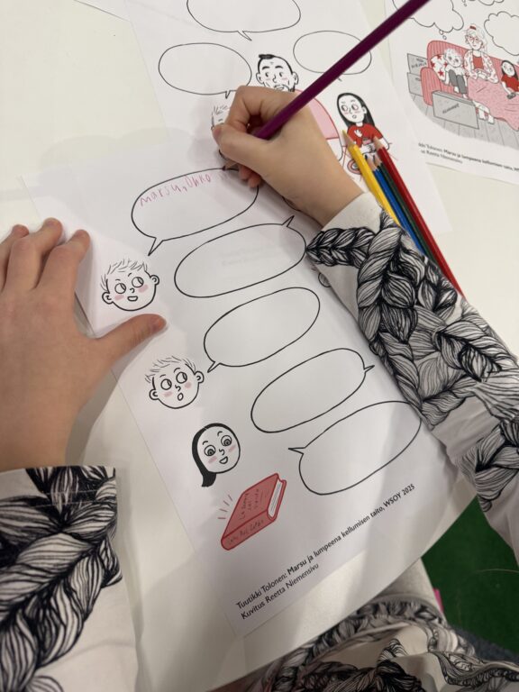 Kuvassa lapsen käsi joka täyttää paperissa olevia puhekuplia.