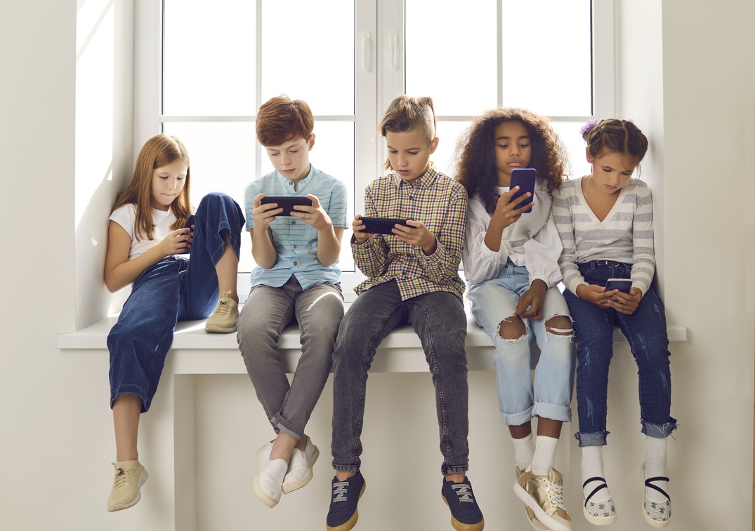 Ryhmä lapsia istuu ikkunalaudalla ja katsoo puhelimiaan,