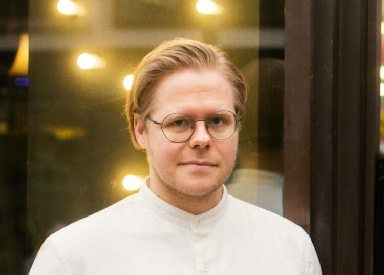 Henkilö katsoo lähikuvassa kameraan. Taustalla on valoheijastuksia.