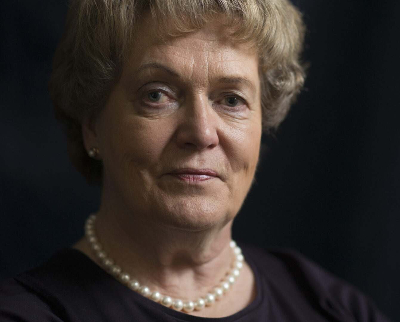 Liisa Keltinkangas-Järvinen katsoo kameraan. Kuvan tausta on tumma, samoin Liisan pusero.