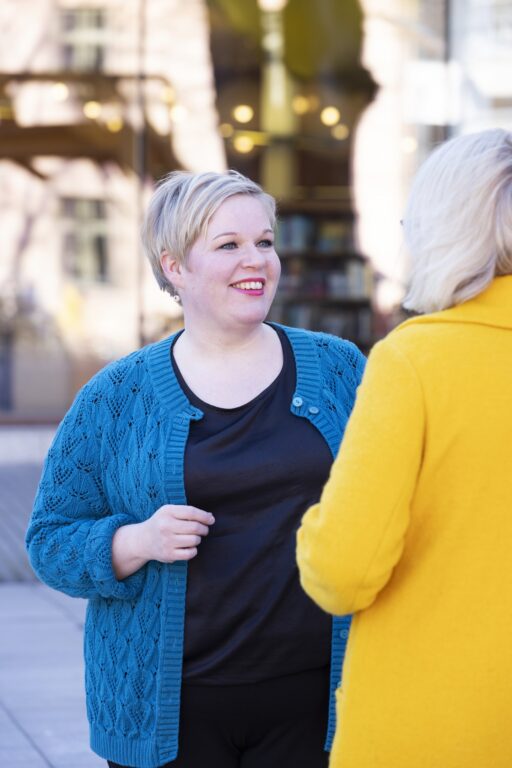 Annika Saarikko seisoo ulkona ja katsoo Kati Leskistä nauraen.