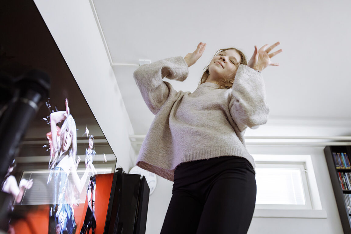 Vauhdikkaassa tanssikuvassa teinityttö tekee K-pop-liikettä omassa huoneessaan kädet ylhäällä. 