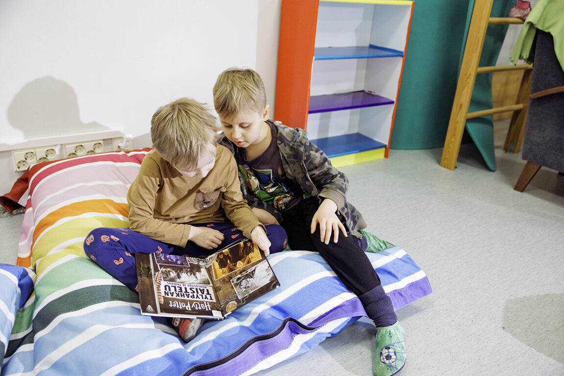 Kuva kahdesta lapsesta, jotka lukevat kirjaa värikkäällä tyynyllä. 