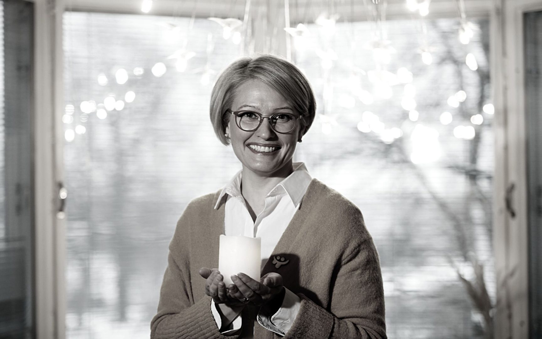 Ulla Siimes katsoo hymyillen kameraan ja pitää kynttilää kädessään.